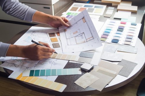 Interior designer working on architectural plans and selecting color swatches for finishes on a table.