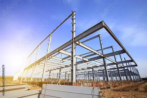 Steel framework of a building under construction with blue skies and sunlight in the background.
